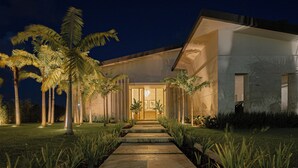 A modern house with a well-lit entrance, a stone pathway leading to the door, and palm trees surrounding the property. - Villa Ametista a Golfer's Dream 5-BD villa in front to Punta Espada Golf Course (Punta Cana)
