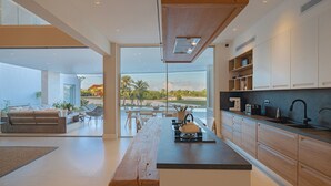 A modern kitchen with a large island, wooden cabinets, and a view of a golf course. - Villa Ametista a Golfer's Dream 5-BD villa in front to Punta Espada Golf Course (Punta Cana)