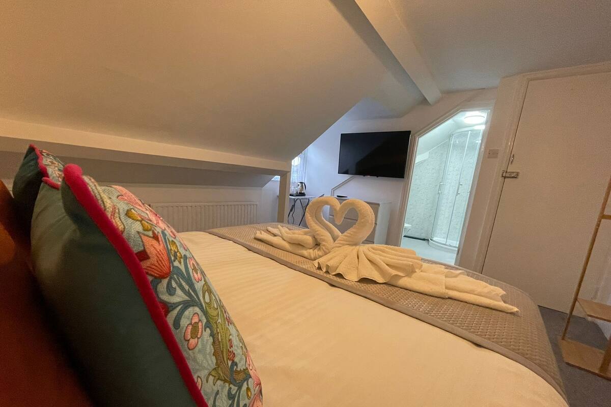 Une chambre d’hôtel avec un lit, un téléviseur fixé au mur et une douche visible à travers la porte.