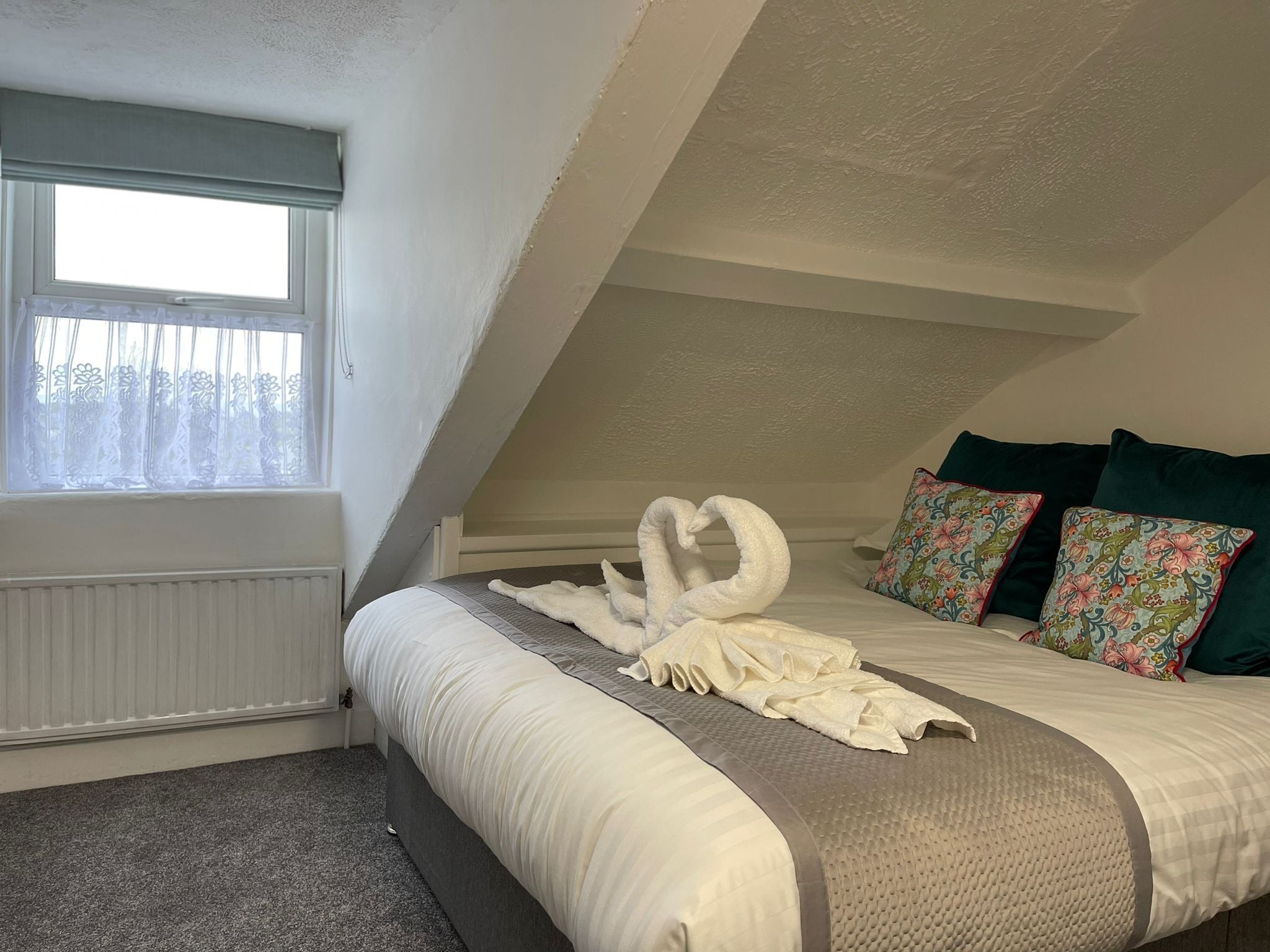 Un dormitorio con cama, ventana con cortinas translúcidas y una composición decorativa de toallas.