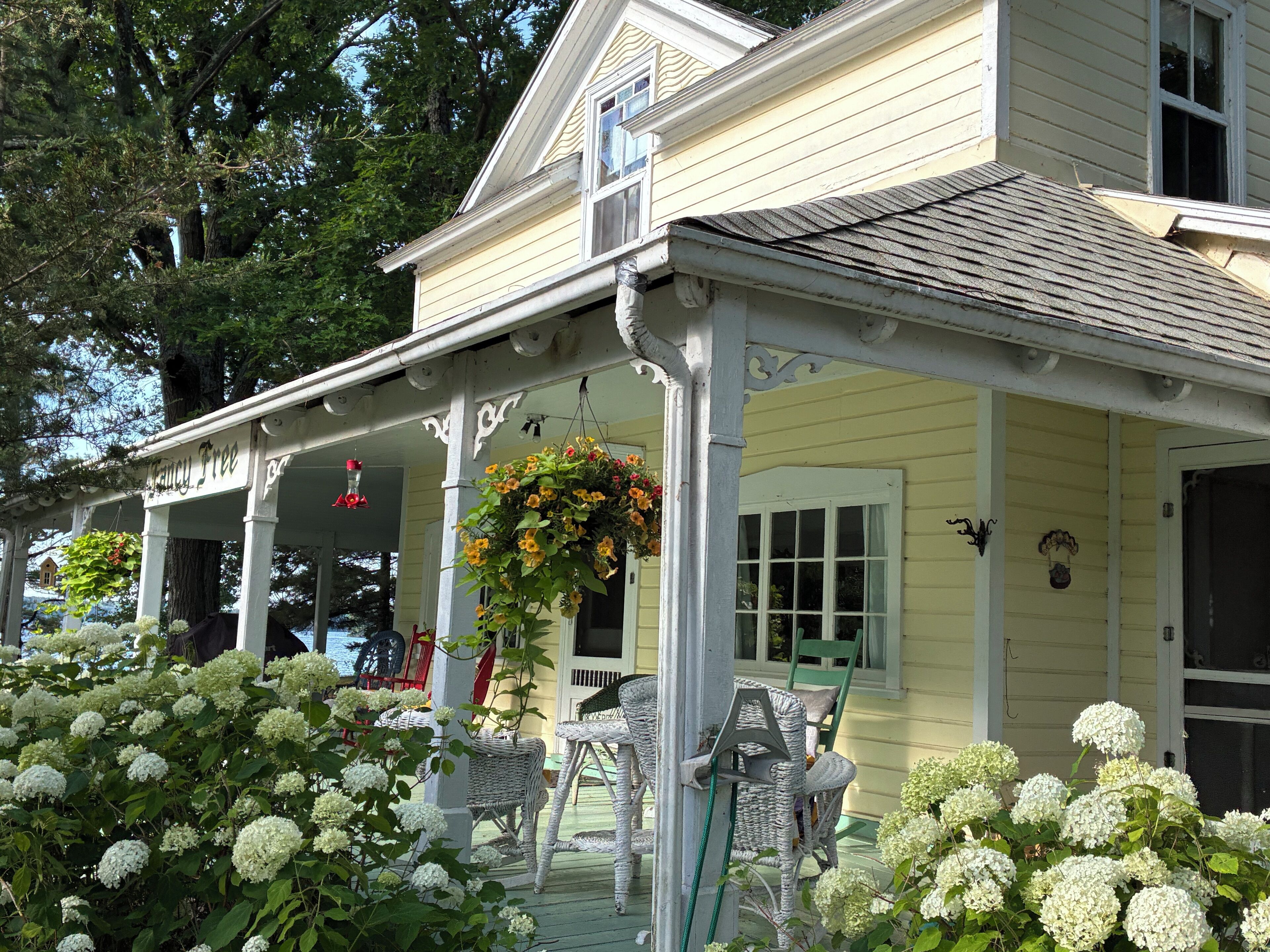 A yellow house with a porch, white wicker furniture, and hanging flower baskets.