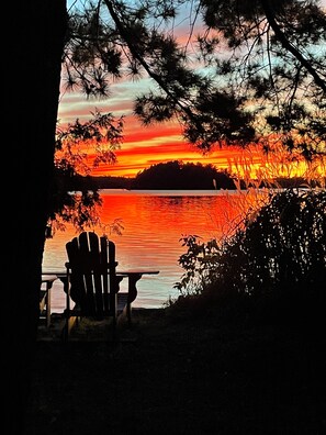 A chair facing a sunset over a body of water, framed by trees. - FANCY FREE ISLAND! Private island paradise, picture perfect Victorian cottage! (Portland)