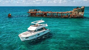 Eine weiße Yacht ankert in der Nähe eines versunkenen Schiffswracks mit klarem, türkisfarbenem Wasser.
