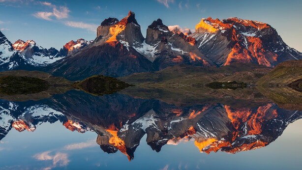 A mountain range with snow-capped peaks and a clear reflection in a body of water. - Sunset Ridge (Early)