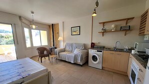 Ein kompakter Wohnbereich mit Sofa, Waschmaschine, Esstisch und Küchenzeile inklusive Mikrowelle und Herd.