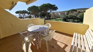 Ein Balkon mit Tisch und Stühlen, gefliestem Boden und Blick auf Bäume und Gebäude.