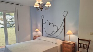 Ein Schlafzimmer mit Bett, Nachttischen, einem Sessel, einer Chandelier und Blick durch eine Glastür.
