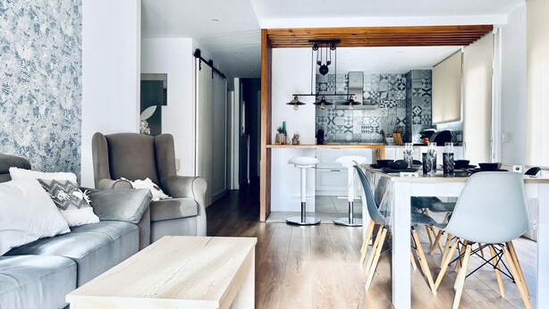 En moderne stue med en grå sofa, et træbord og et spiseområde med et hvidt bord og stole.