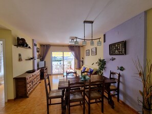 A dining area with a wooden table and chairs, a TV on a cabinet, and a sliding glass door leading to an outdoor patio. - 3-bedroom apartment with terrace near the beach (L'Escala)