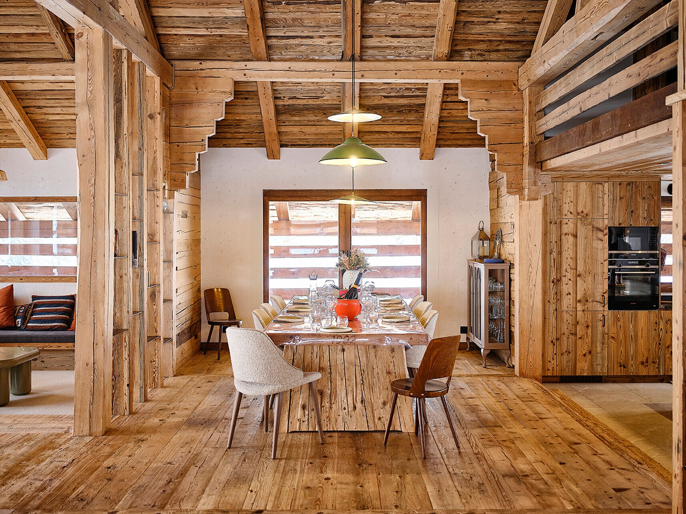 Un intérieur rustique en bois, avec une table à manger pour six personnes, des poutres apparentes au plafond et des appareils électroménagers intégrés.