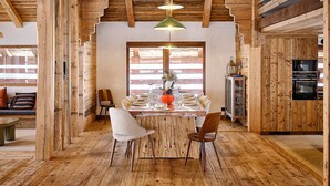 Ein rustikales Holzinterieur mit einem Esstisch für sechs Personen, Holzbalken an der Decke und eingebauten Geräten.