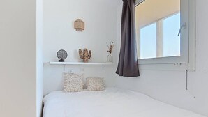 Et soveværelse med en seng, et vindue med gardiner, en reol med dekorative genstande og en vægmonteret lampe.