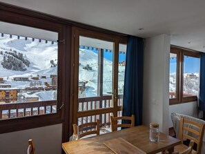 A dining area with a wooden table and chairs, large windows with a view of a snowy mountain landscape. - 2-room Apt, Plagne Centre, 5 ppl, slope view (La Plagne)