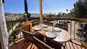 Un balcón con una mesa lista para comer, con vista al mar y edificios, y palmeras.