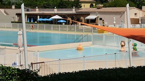 Una piscina con un puesto de salvavidas, una sombrilla y un juguete inflable pequeño.