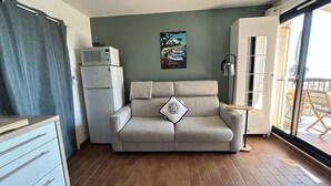 Un espacio habitable compacto con sofá, un mueble pequeño, microondas y un cuadro en la pared.