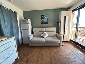 Ein gemütlicher, kompakter Wohnraum mit einer Couch, einem kleinen Schrank, einer Mikrowelle und einem Bild an der Wand.