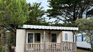 A small, single-story cabin with a wooden deck and a covered porch. - Family Mobile Home: 3 Rooms, Sleeps 4 (SAINT-HILAIRE-DE-RIEZ)