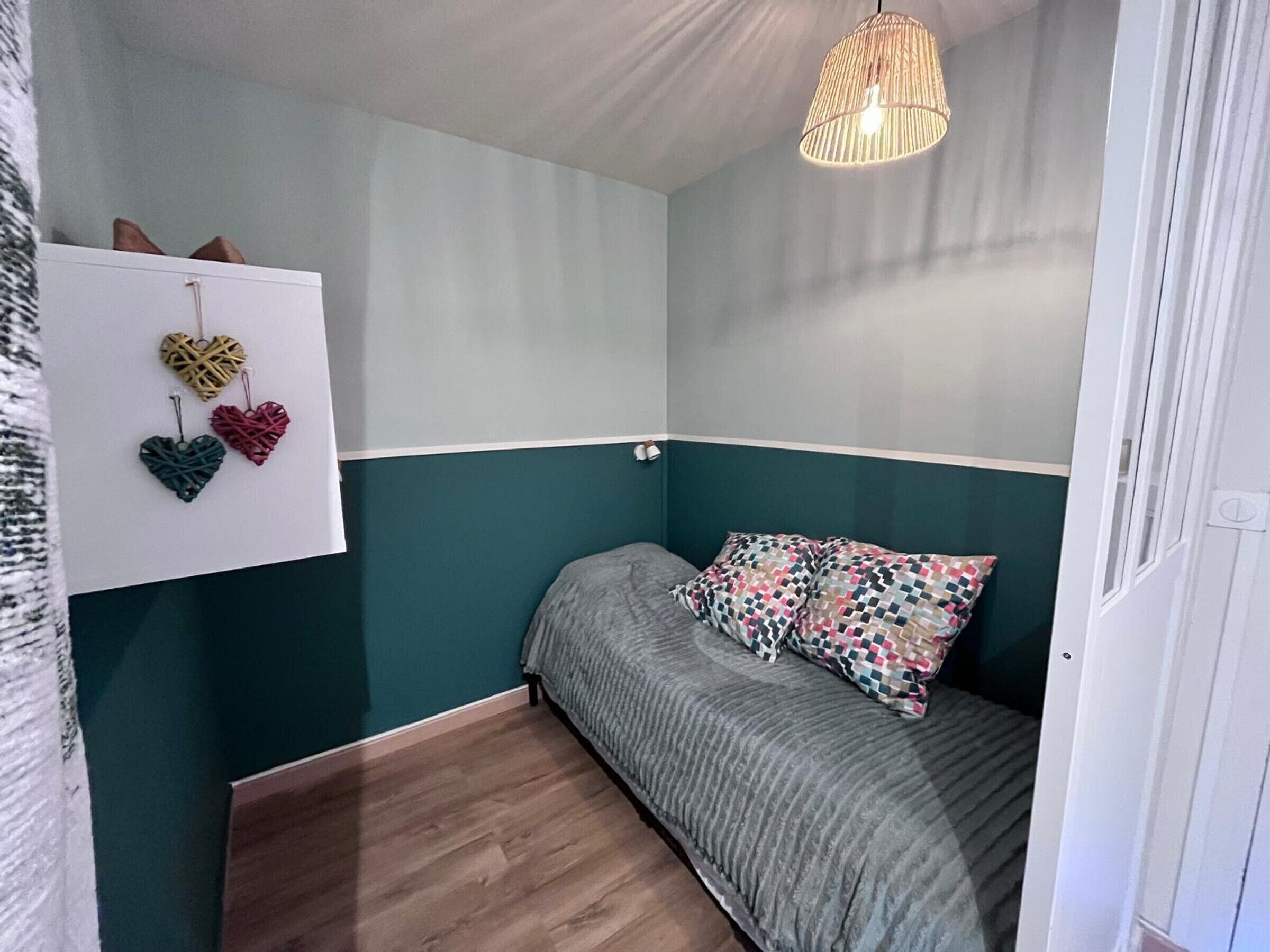 Un dormitorio con una cama, una lámpara colgante y un estante en la pared con adornos con forma de corazón.