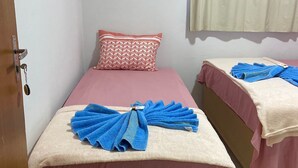 Une petite pièce, bien rangée, avec deux lits, chacun recouvert d’une couverture rose et agrémenté de serviettes bleues.