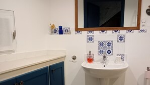 Casa de banho com uma pia branca, armários azuis, um cesto de lixo branco e uma cesta de vime.
