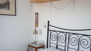 Uma cama bem arrumada com um edredom branco, uma pequena mesa de cabeceira com abajur e um quadro na parede.