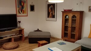 Uma sala de estar com televisão, sofá, mesa de centro, armário e um quadro na parede.