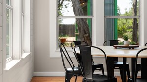 A dining area with a table and chairs, a window with a view of trees and a building, and a potted plant on the table. - Tranquil 4BR Retreat on 2 Acres w/ Boat Dock – Lago Vista (Lago Vista)