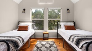 A room with two beds, a small table, and a view of trees through large windows. - Tranquil 4BR Retreat on 2 Acres w/ Boat Dock – Lago Vista (Lago Vista)