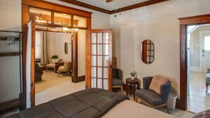 Ein Schlafzimmer mit Bett, Stuhl, kleinem Tisch, Deckenventilator und einer Schiebetür zu einem anderen Raum.