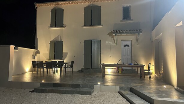 Ein Gebäude mit einer Terrasse, die einen Tisch und Stühle, eine Tür und ein kleines Fenster zeigt.