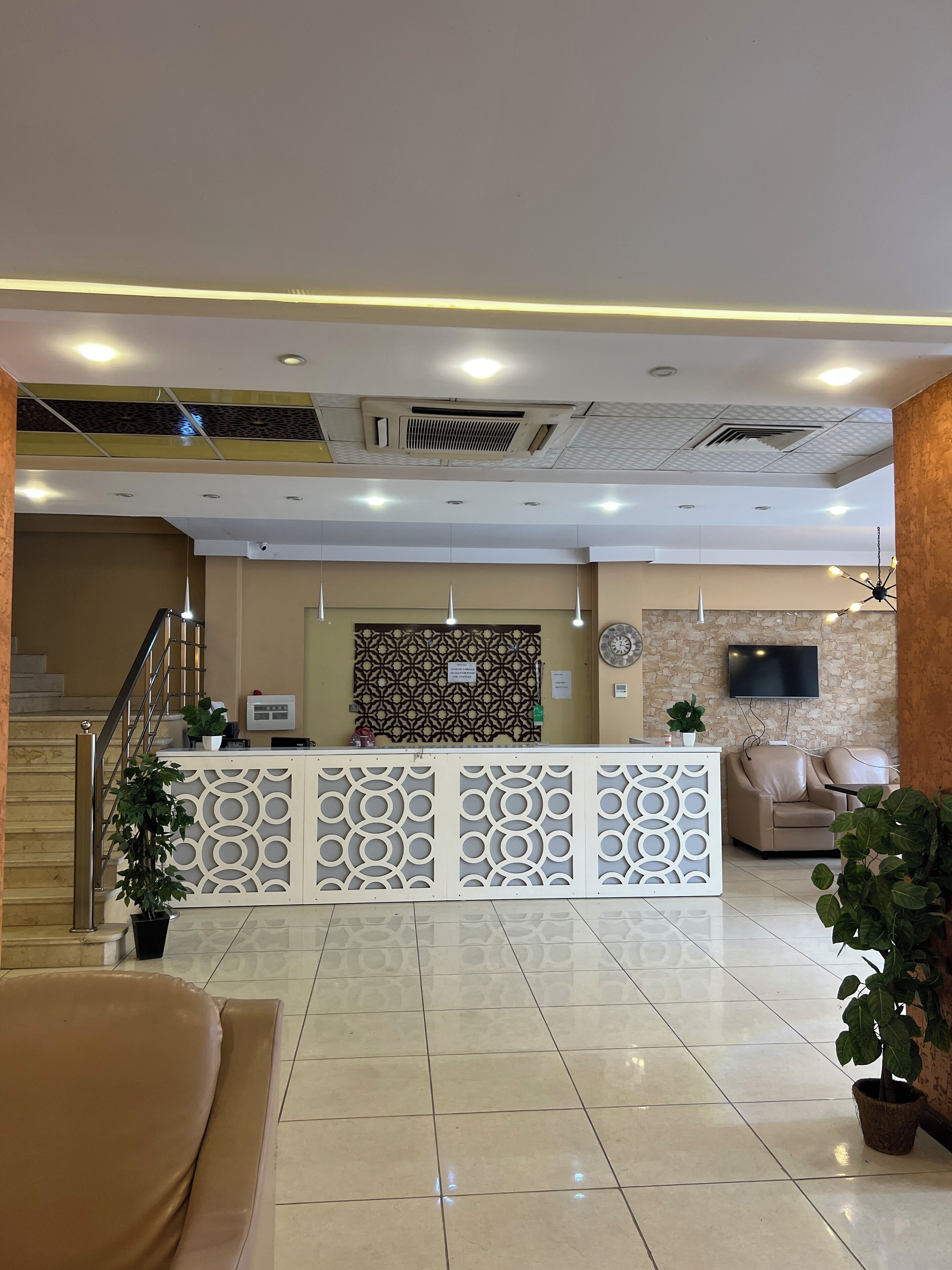 A hotel reception area with a reception desk, seating area, and a staircase.