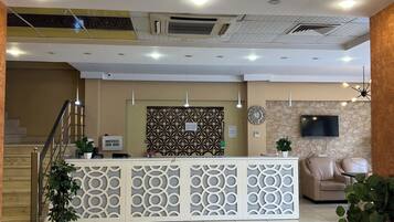 A hotel reception area with a reception desk, seating area, and a staircase.