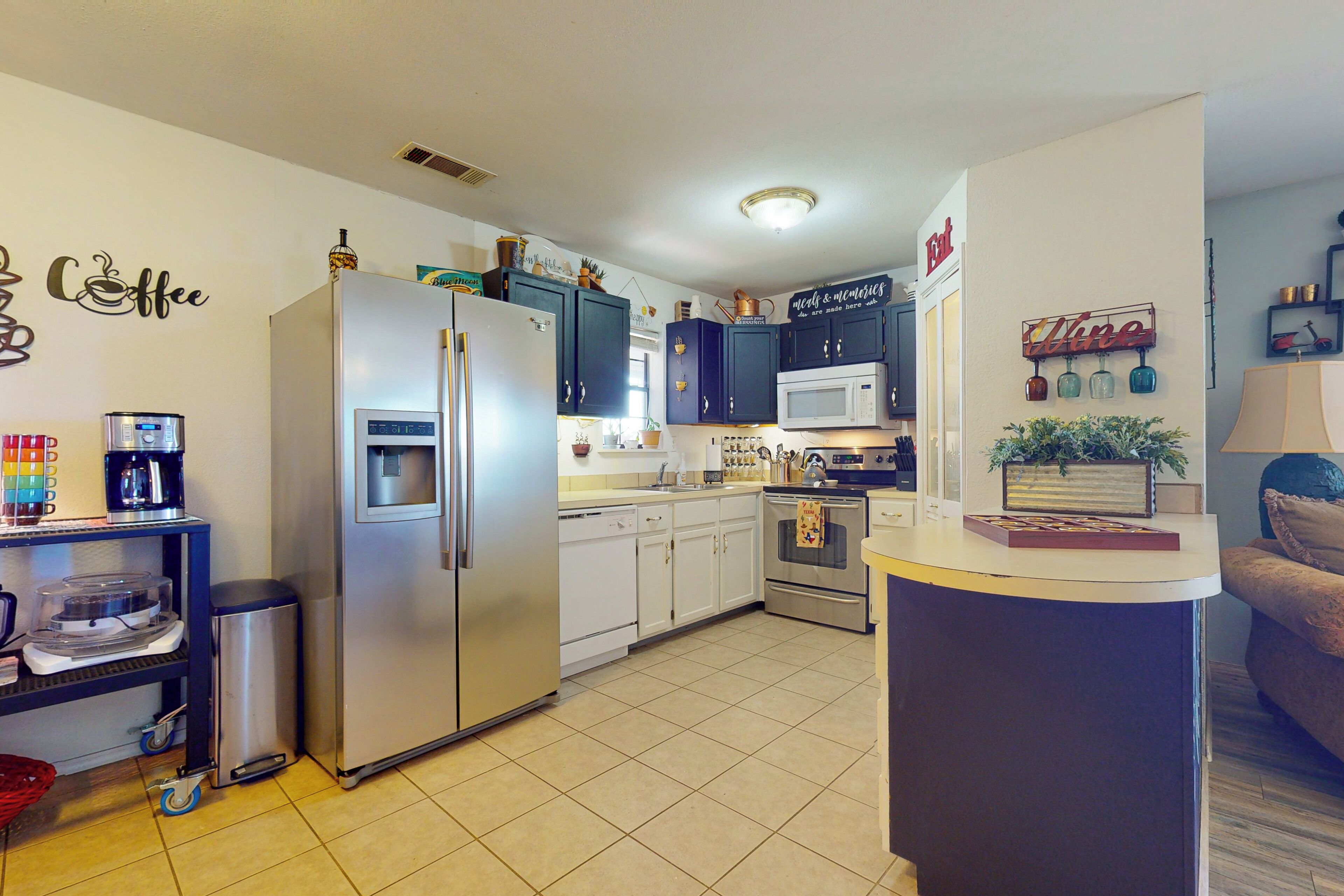 A compact kitchen with a refrigerator, microwave, and stove. There are cabinets, a sink, and a coffee machine.