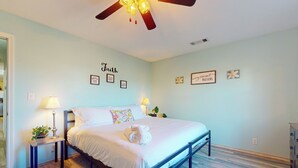 Un dormitorio con cama, dos mesitas de noche, ventilador de techo y adornos en la pared.