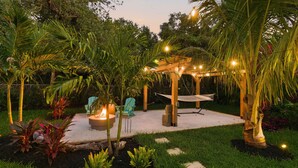 Un espace patio agrémenté d’une pergola en bois, de guirlandes lumineuses, d’un foyer extérieur et de mobilier de jardin.