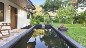 Une maison avec un petit étang, un banc et un arbre en pot.