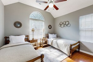 Ein Schlafzimmer mit zwei Betten, einem Deckenventilator, einem großen Fenster mit Jalousien und einem Holzboden.