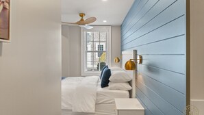 Ein Schlafzimmer mit einem Bett, einem Nachttisch, einem Deckenventilator und einem Fenster mit Jalousien.