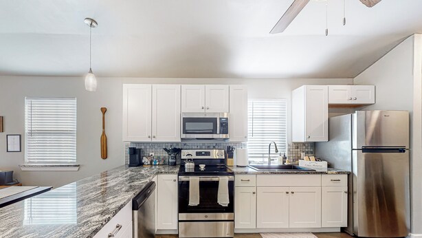 A modern kitchen with white cabinets, stainless steel appliances, granite countertops, and a wooden ceiling fan. - Steps to Lake Eufaula: Home w/ Fire Pit & BBQ (Eufaula)