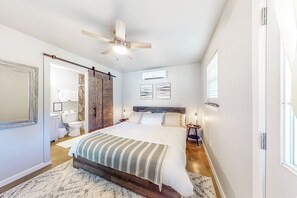 A bedroom with a large bed, a ceiling fan, a wooden floor, and a bathroom visible through an open door. - Steps to Lake Eufaula: Home w/ Fire Pit & BBQ (Eufaula)