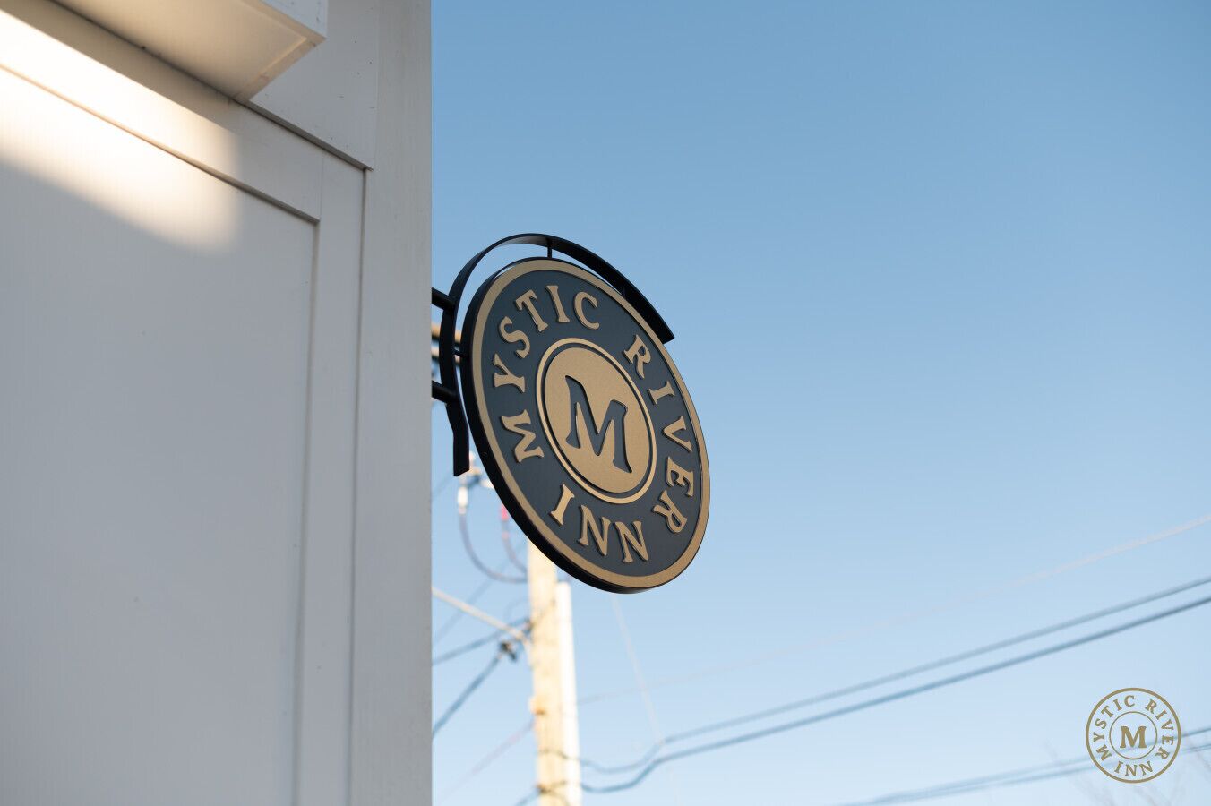 A circular sign with the text "Mystic River Inn" and a prominent 'M' logo.