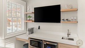 A modern kitchen with a flat-screen TV, wooden shelves, a microwave, and a sink.