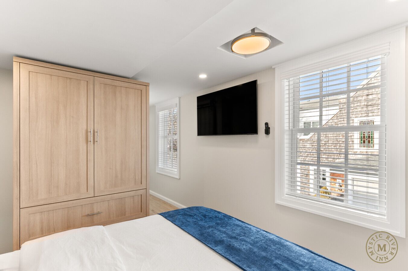 A bedroom with a bed, a wardrobe, a TV, and a window with blinds.