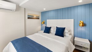 Une chambre à coucher comprenant un lit, une table de chevet, une lampe fixée au mur et un appareil de climatisation.