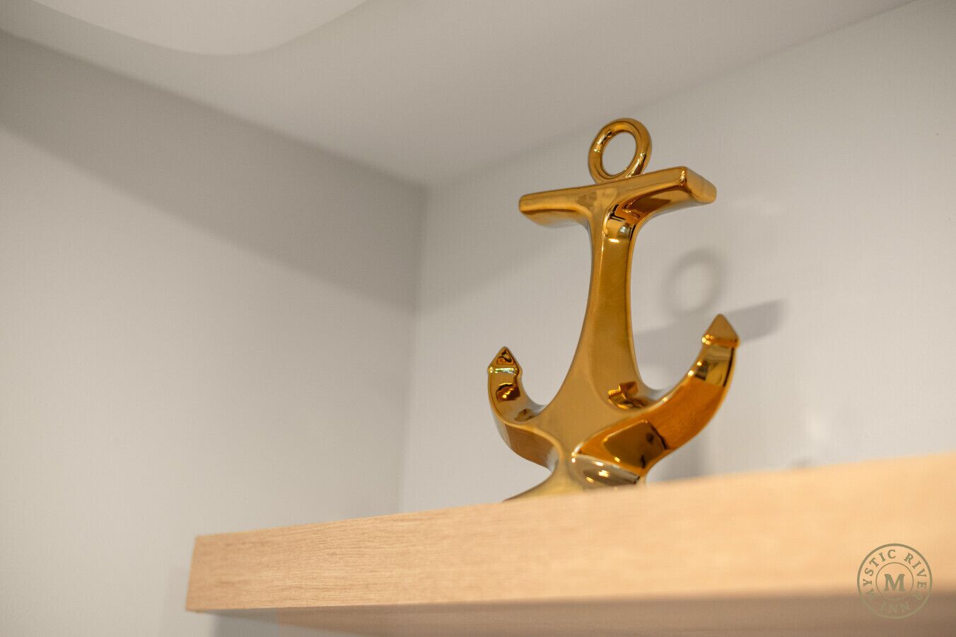 Un ancla dorada sobre una estantería de madera frente a una pared lisa.