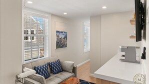 Une chambre d’hôtel moderne, dotée d’un canapé, d’une machine à café et offrant une vue sur la ville grâce à de grandes fenêtres.