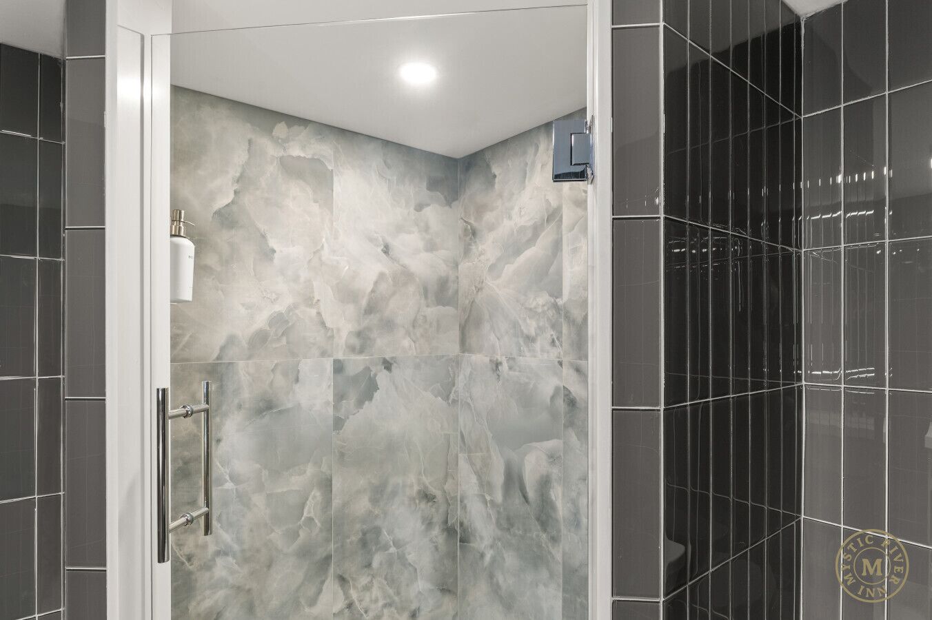 A modern bathroom with a marble wall, a glass shower enclosure, and a black tiled wall.