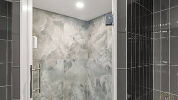 A modern bathroom with a marble wall, a glass shower enclosure, and a black tiled wall.
