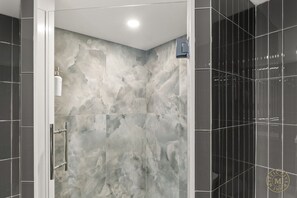 A modern bathroom with a marble wall, a glass shower enclosure, and a black tiled wall. - The Mystic River Inn (Groton)
